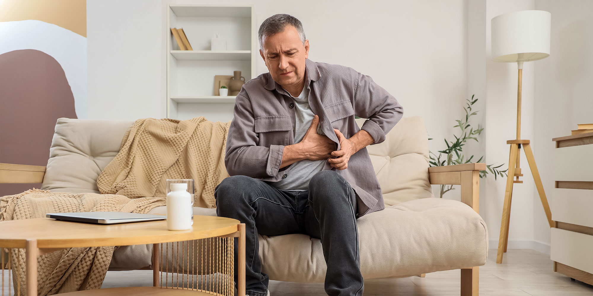 Mature man suffering from chest pain on sofa at home