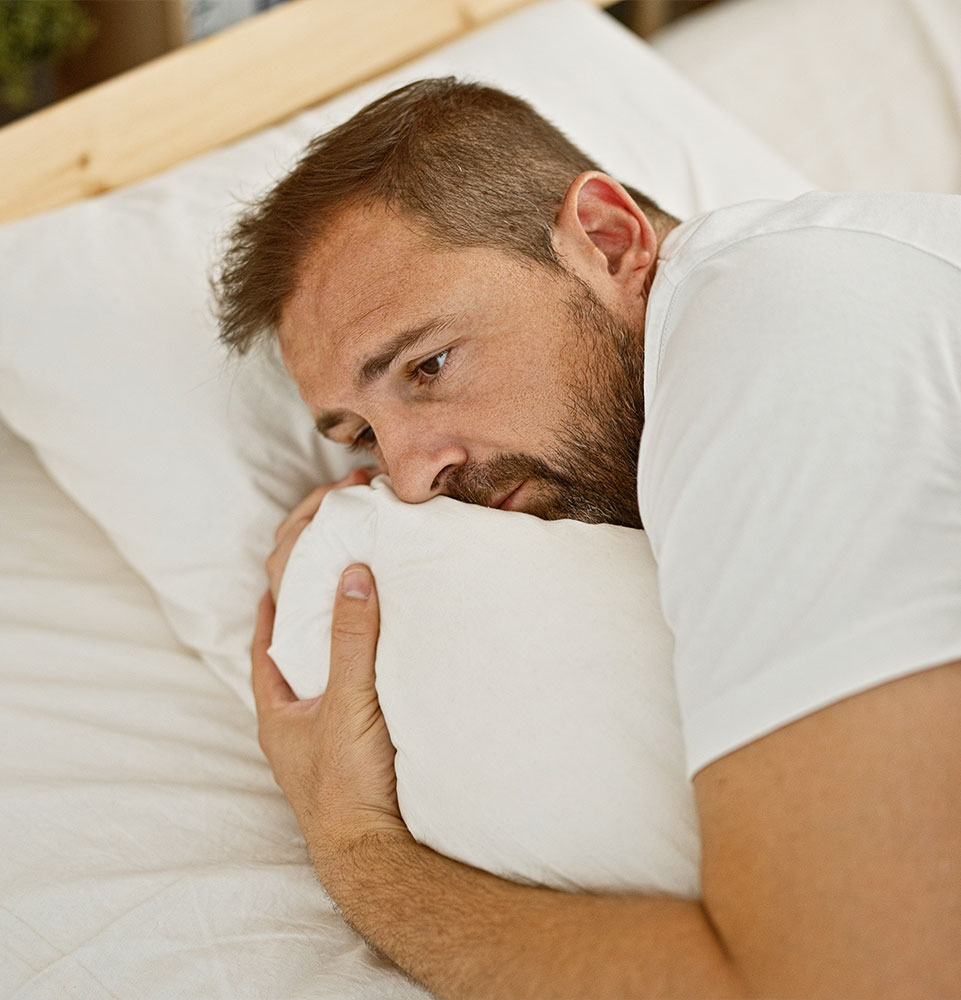 Worried middle-aged man with grey hair lying in bed indoors, portraying anxiety or insomnia